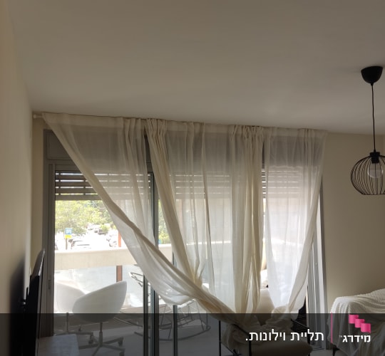 וילון לבן תלוי על חלון זכוכית גדול
